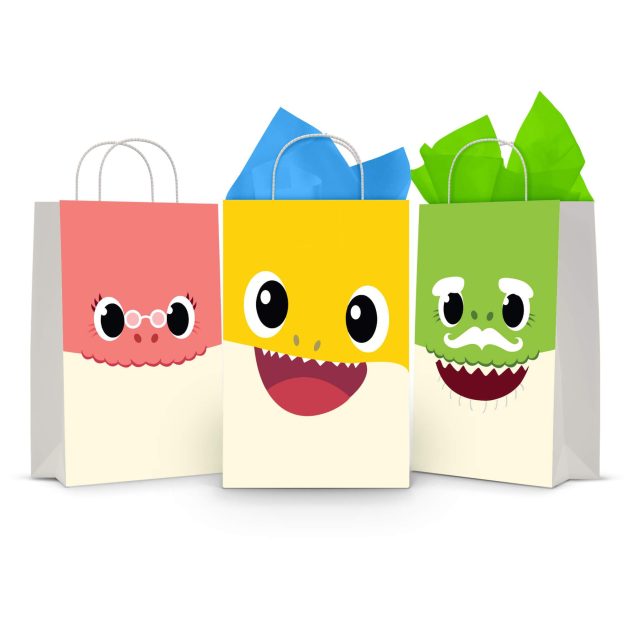 Three printable Baby Shark goodie bag fronts on paper party bags — the big-face designs for Grandma Shark on rose, Baby Shark on yellow and Grandpa Shark on green.