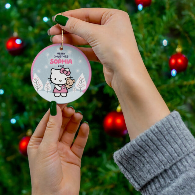 Hello Kitty in a red dress holding her teddy in a blue winter village - custom name Christmas ornament