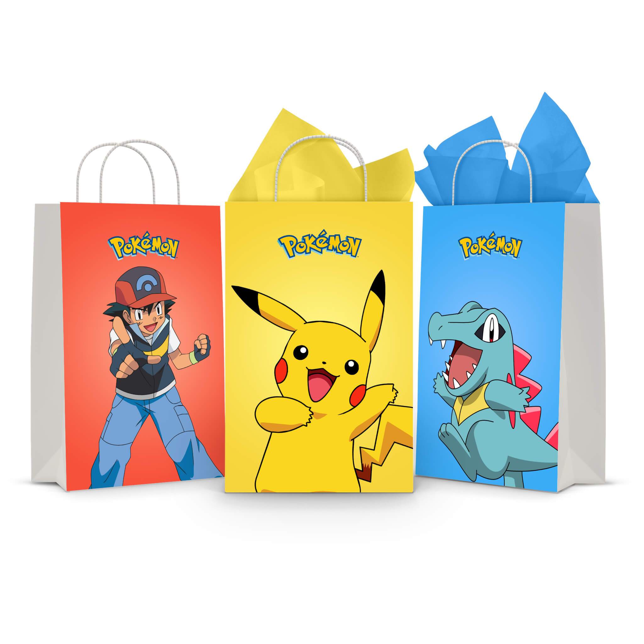 Three printable Pokemon goodie bag fronts on paper party bags — Ash Ketchum on red, Pikachu mid-cheer on yellow and Totodile on blue, each topped with the Pokemon logo.