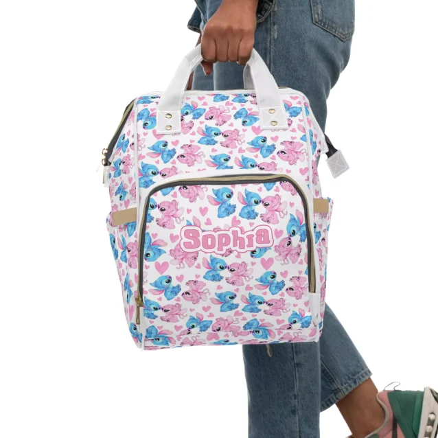 A white diaper bag with pink and blue accents, featuring characters from the Disney movie Lilo & Stitch. Perfect for adventures with your little one!