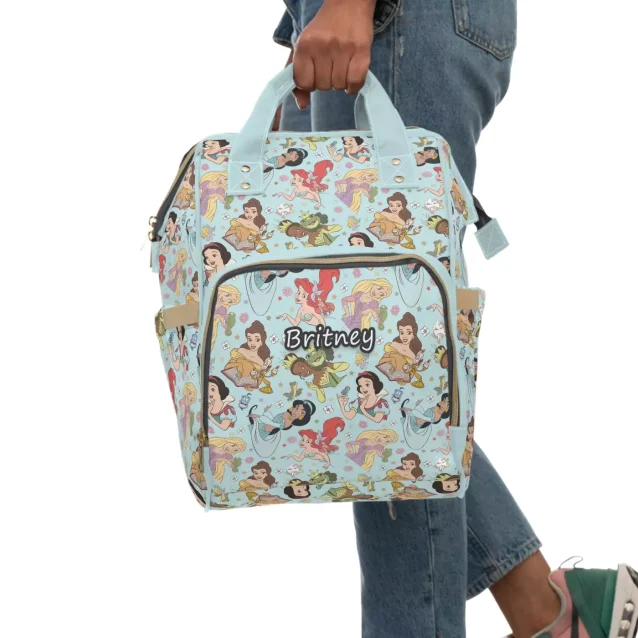 A flat lay of the Disney Princess Diaper Bag and its contents, including wipes, diapers, and toys.
