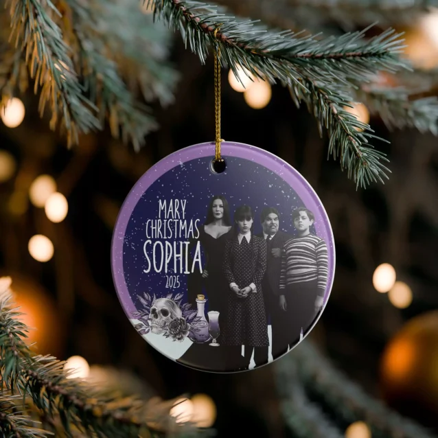 A hand placing a Wednesday Addams ornament on a black Christmas tree.